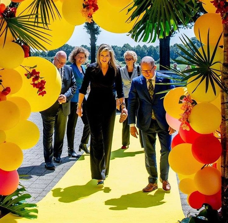 Koninging maxima loopt dor een kleurrijke balonnenboog gemaakt door Cobi